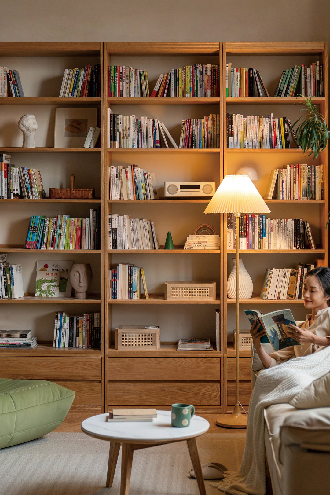 Woman reading a book in a cozy living room with a large wooden bookshelf.