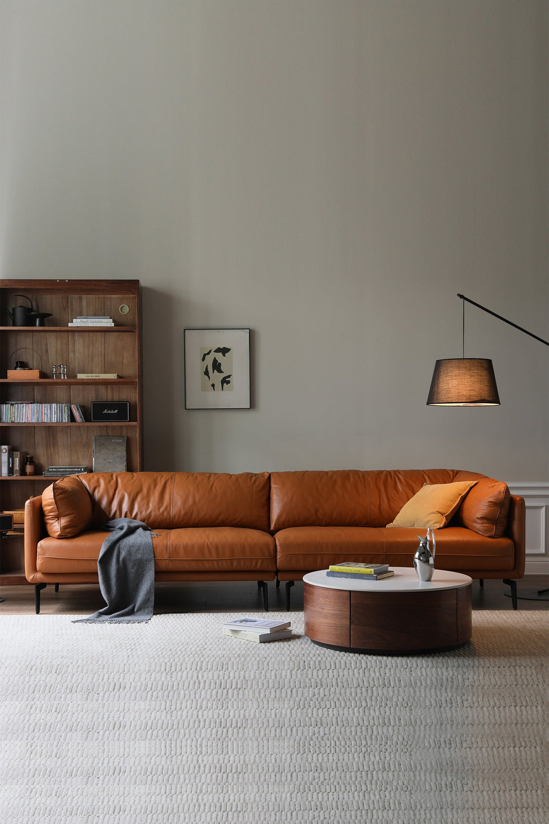 Modern living room with a brown leather sofa, round wooden coffee table, and bookshelf.