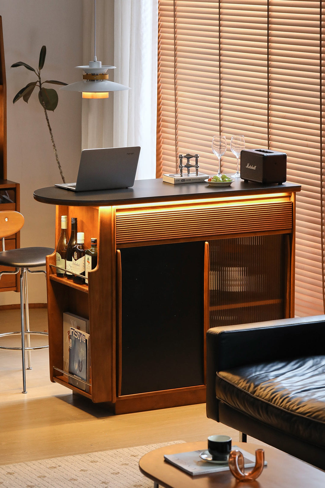 Wooden bar table with a laptop, bottles, and a coffee cup in a home setting.