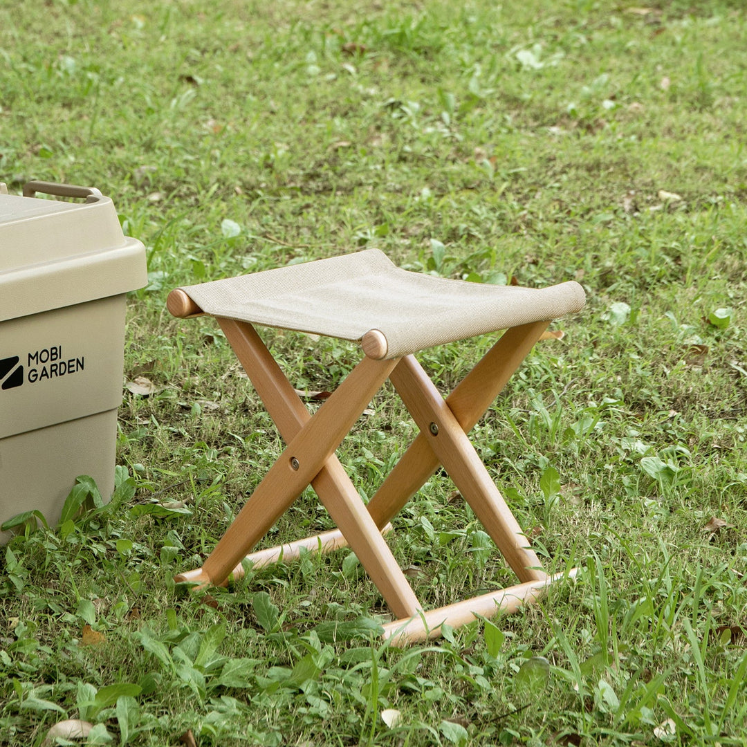 Compact foldable stool with a sturdy wooden frame and beige fabric seat, perfect for outdoor use, enhancing portable and convenient seating solutions.