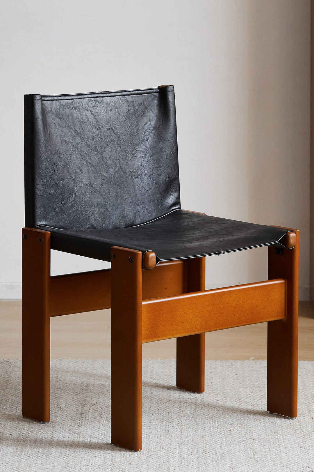 Chair with a black leather seat and backrest on a wooden frame, placed on a light-colored floor. Featured in Loft Home Singapore's leather chairs collection.