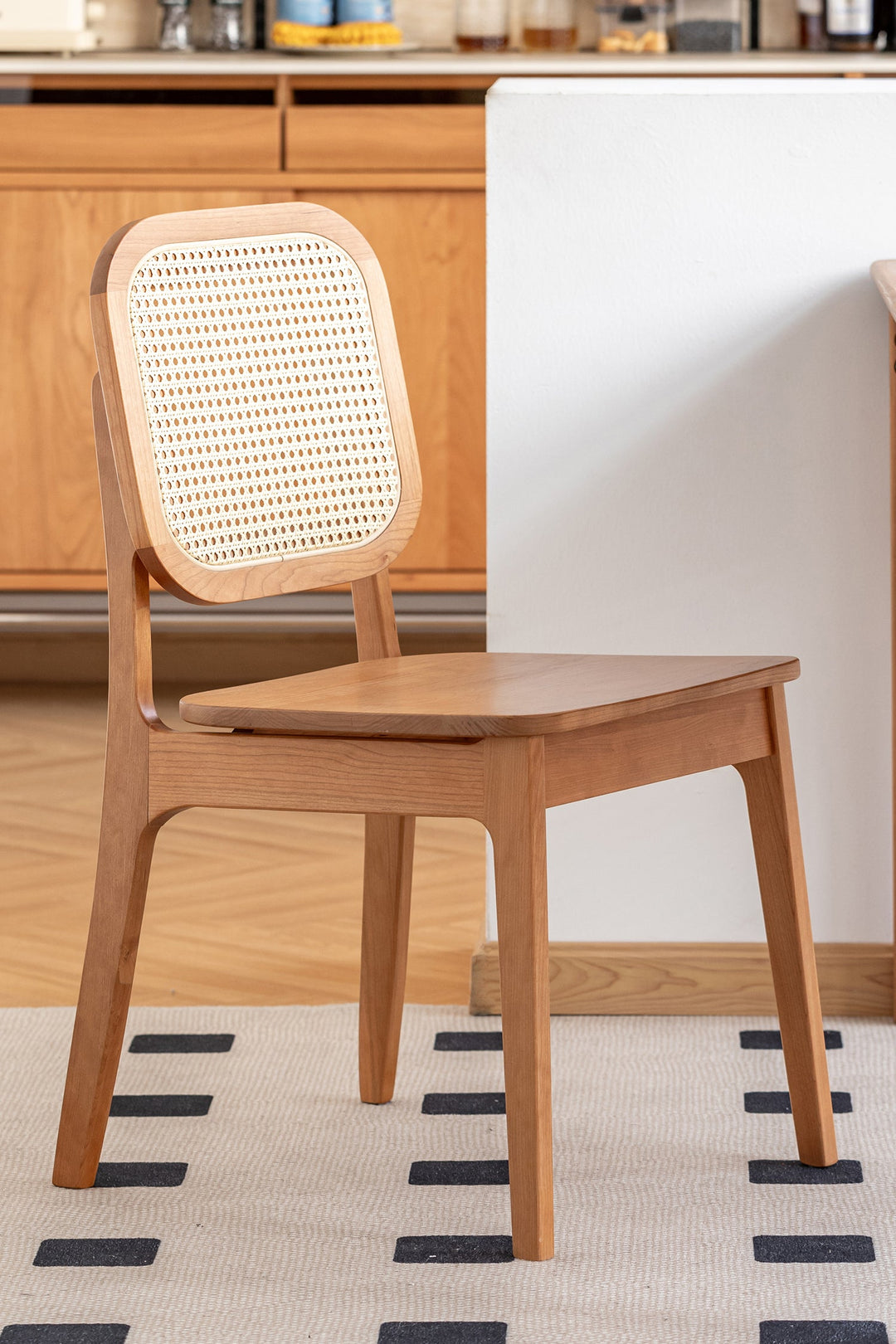 Rattan chair with wicker backrest in a room with wooden cabinets and a rug. Featured for Loft Home Singapore's rattan chairs collection.