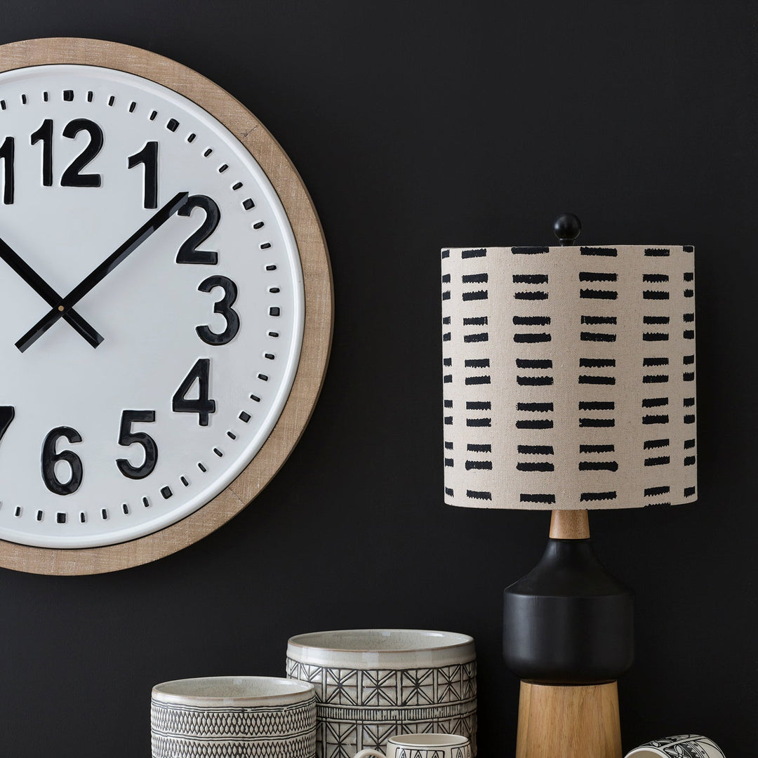 Decor setup featuring a large wall clock, patterned table lamp, and ceramic containers, blending modern and rustic styles for a chic look.