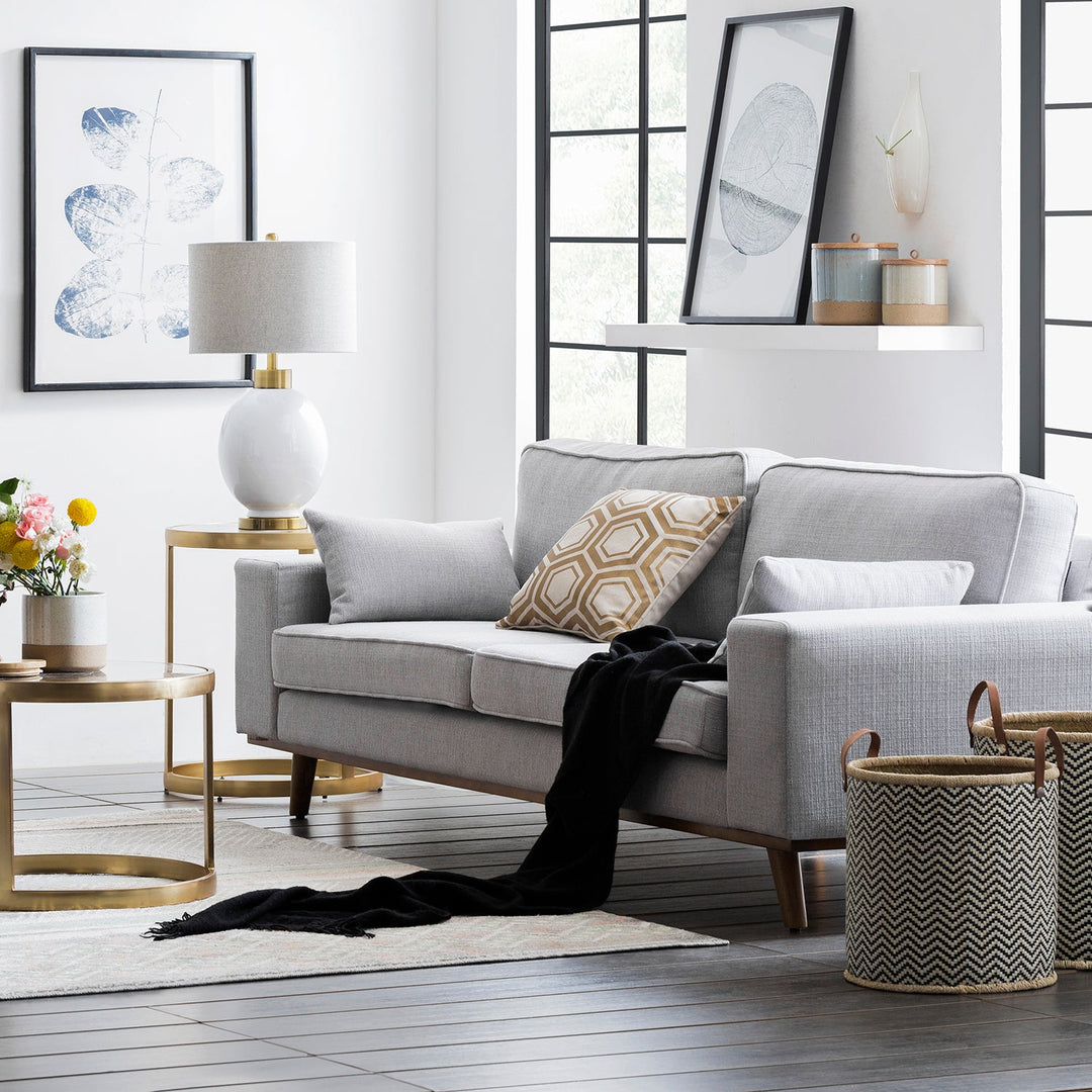 Loft Home top-selling grey fabric sofa, styled with a geometric cushion and modern brass side tables, enhancing elegant and functional living room decor.