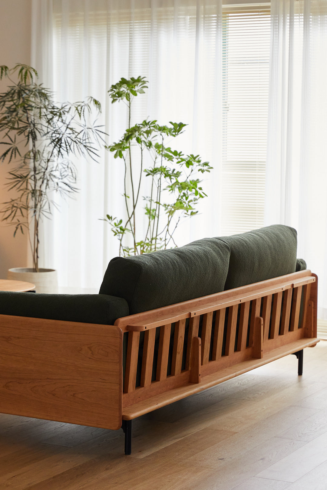 Wooden sofa with green cushions in a room featuring large windows and plants. Showcased for Loft Home Singapore wooden sofas.
