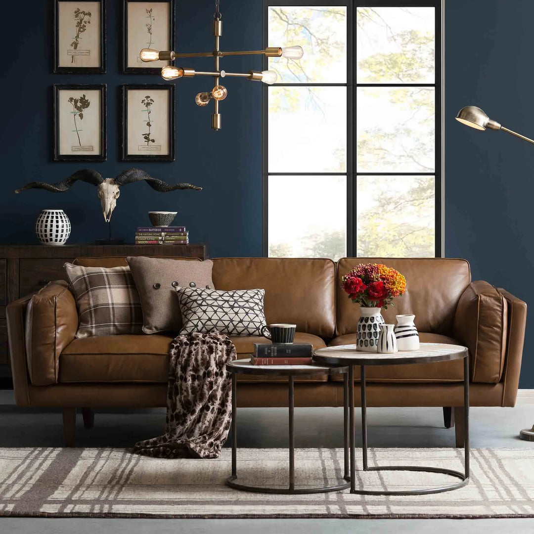 Featured in Loft Home's 3-seater sofa collection, cozy living room with a brown leather 3-seater sofa, modern coffee tables, and decorative elements including wall art and a skull sculpture.