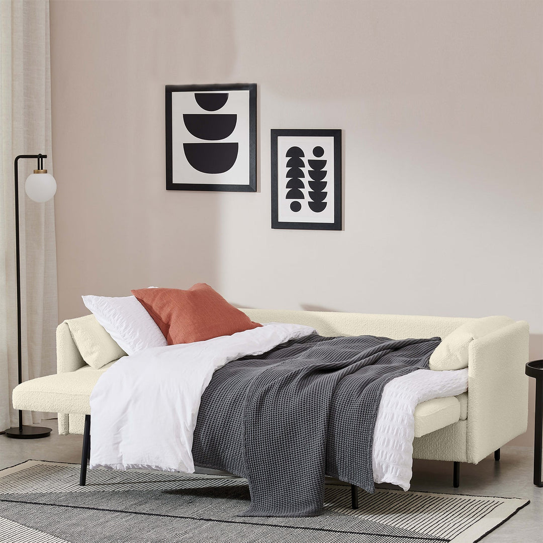 Modern sofa bed with cozy bedding, abstract wall art, and minimalist decor, offering a stylish and practical solution for small living spaces.