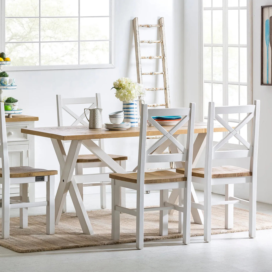 Bright and airy dining room with a cream-colored wooden table and matching chairs, complemented by rustic decor elements and large windows, perfect for a fresh and inviting home interior.