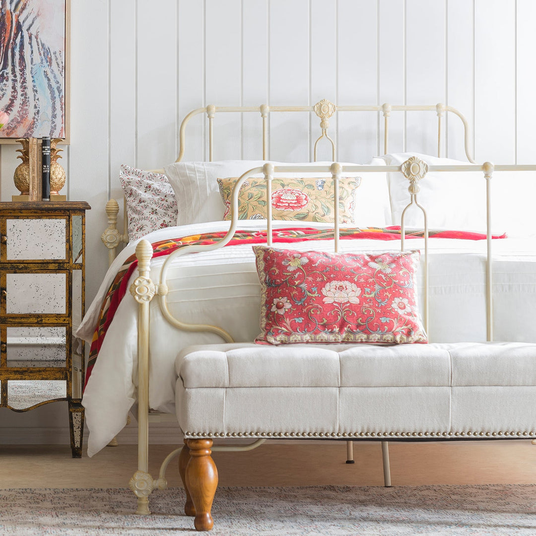 Elegant bedroom with a minimalist metal bed frame, floral pillows, and a tufted bench, blending vintage charm with modern simplicity.