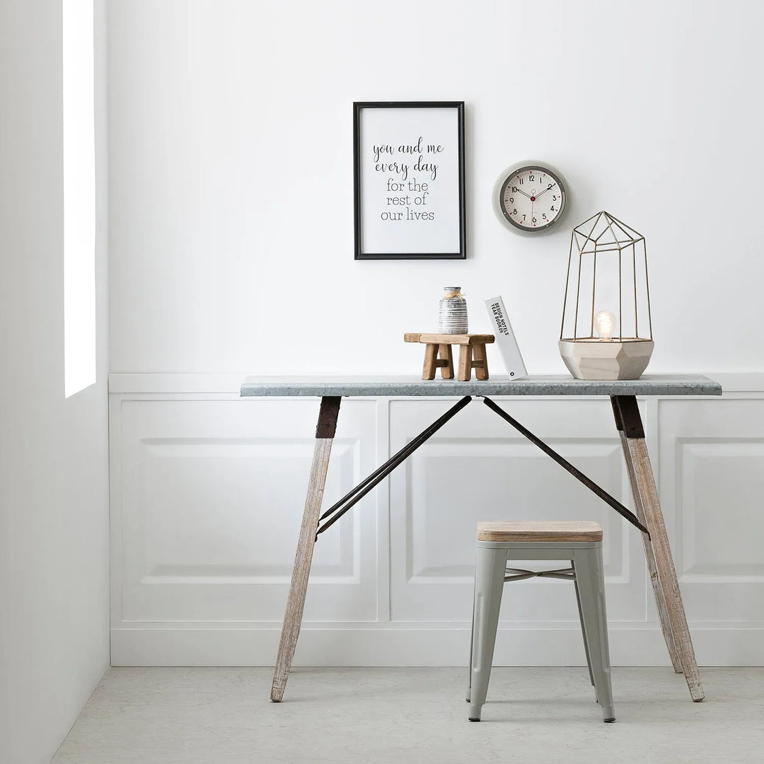 Minimalist home office setup with a sleek table featuring metal legs and wooden accents, a modern stool, a decorative lamp, and wall art with a motivational quote - ideal for a contemporary minimalist aesthetic.