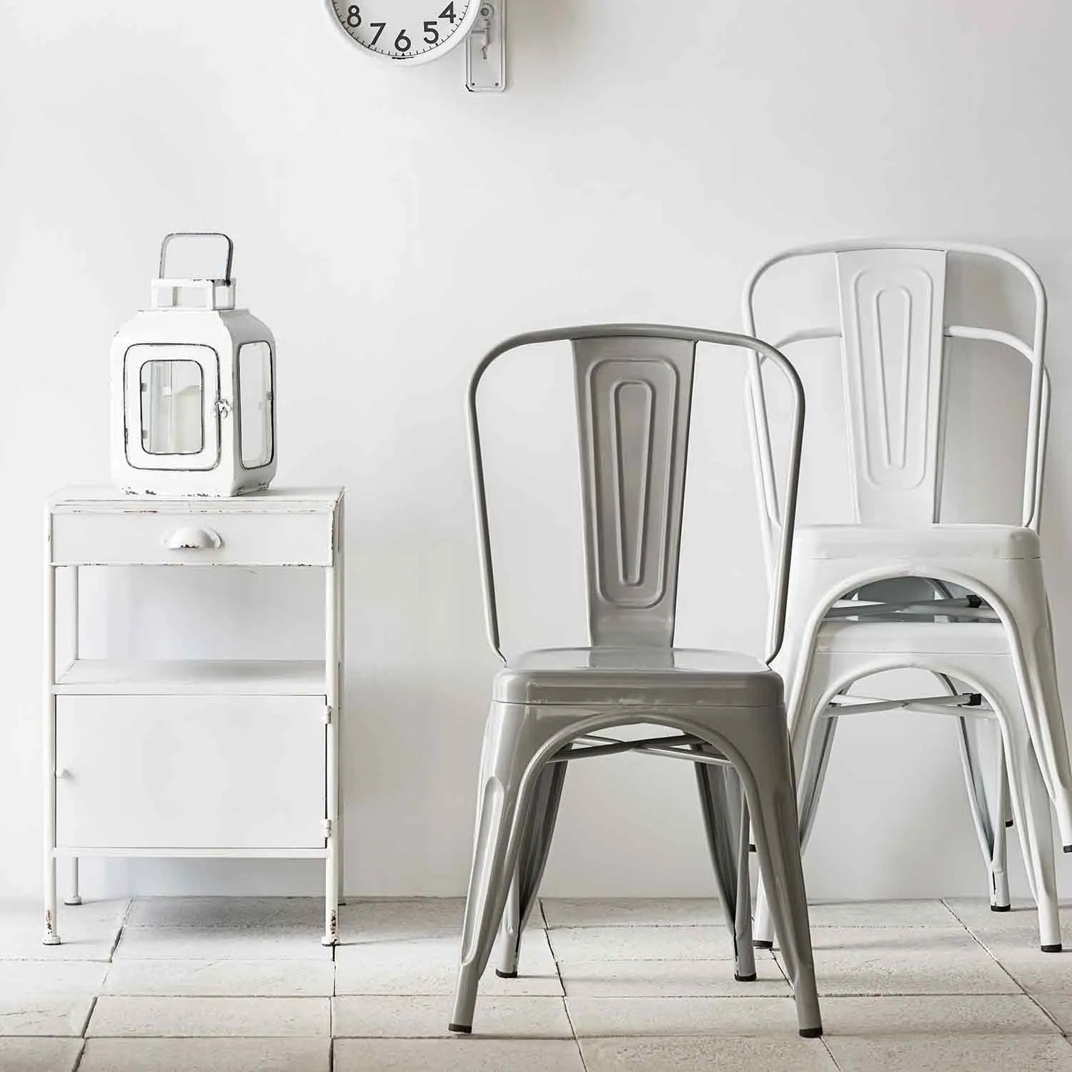 Featured in Loft Home's chairs collection: Minimalist setup with metal dining chairs, a rustic side table, and a vintage wall clock.