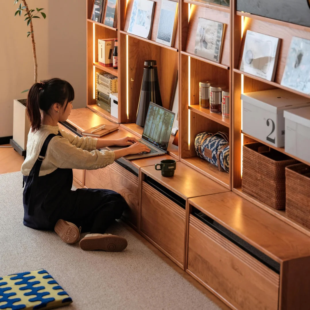 Cherry wood bookshelf with built-in drawers and integrated LED lighting, offering versatile storage and a cozy workspace setup.