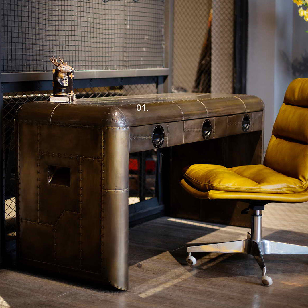 Loft Home Brass Tables collection, showcasing an industrial-inspired brass desk with riveted details, perfectly pairs with a yellow leather chair for a bold statement.