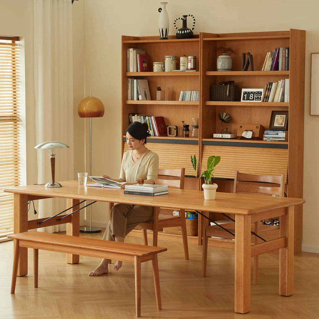 Loft Home cherry wood furniture collection featuring a woman reading at a wooden table with matching bench and bookshelf in a cozy setting.