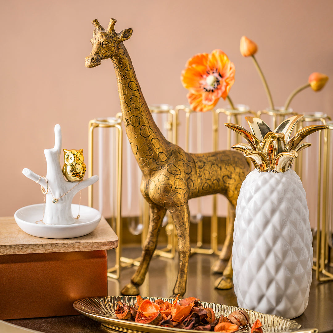 Loft Home decorative accents featuring a gold giraffe, a white pineapple vase, and a golden owl figurine in a stylish and modern setting.