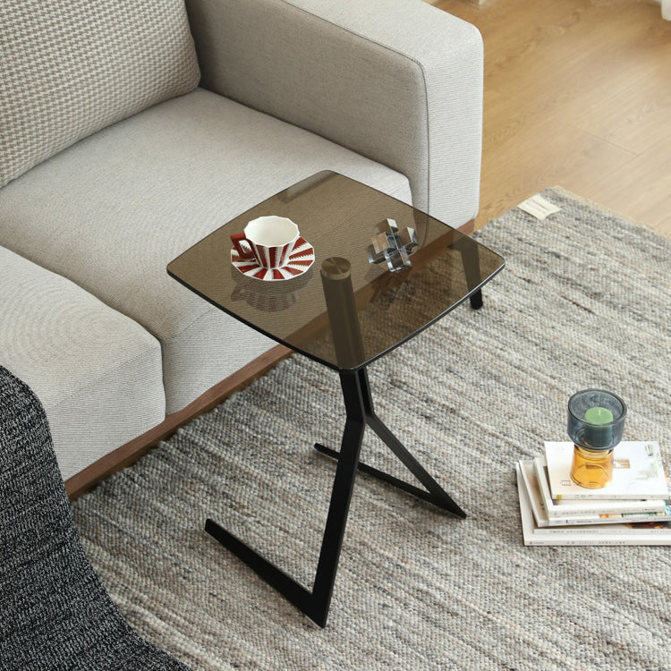 Contemporary glass side table with a sleek black metal base, ideal for modern living room spaces, styled with a cup and books for functionality.