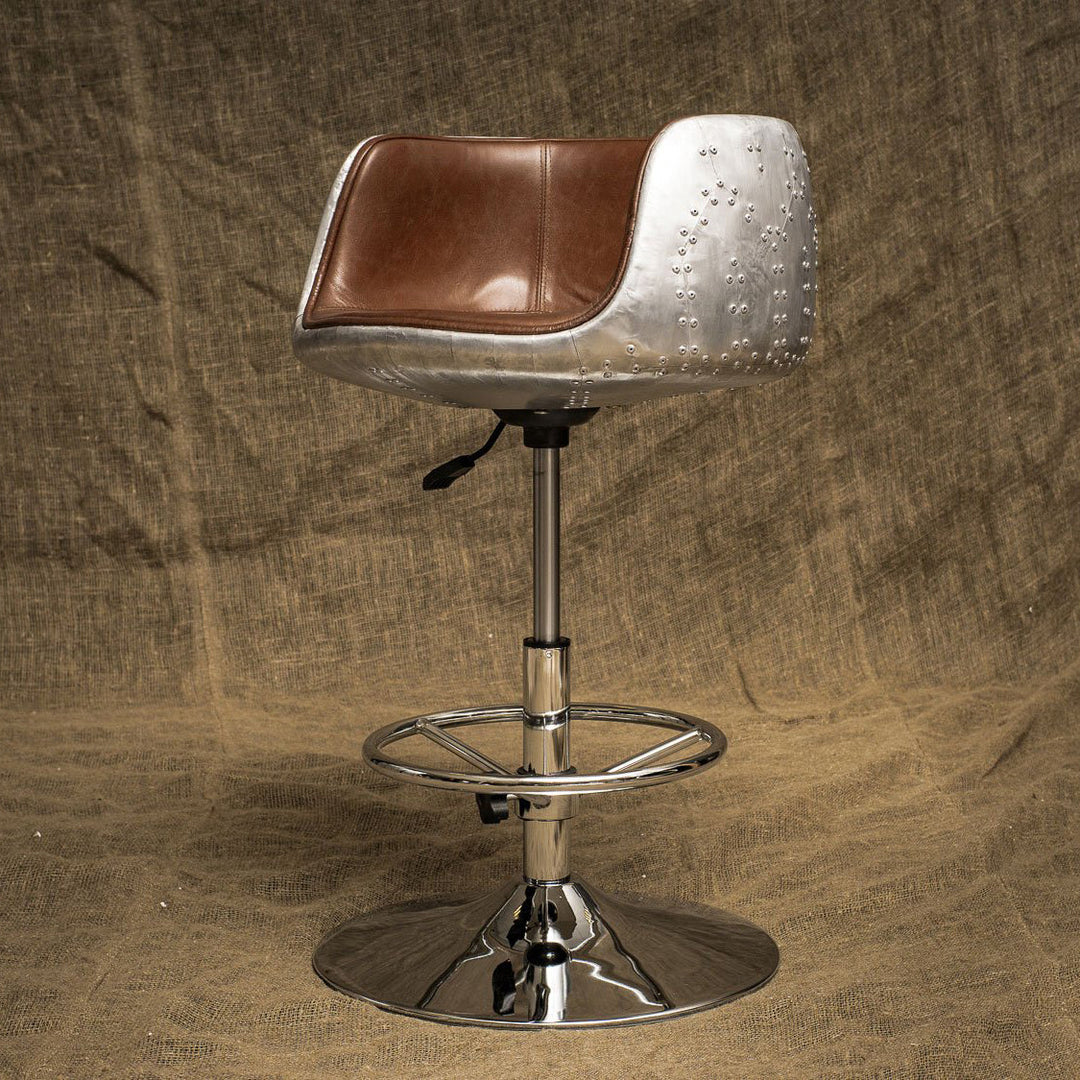 Industrial-style bar chair with a riveted aluminum frame and brown leather seat, featuring an adjustable chrome base, ideal for lofts or modern bar setups.