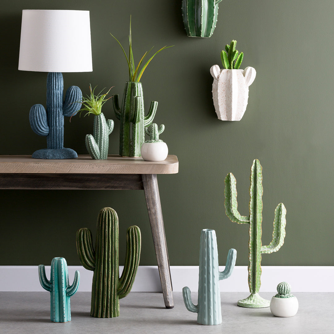 Assorted ceramic cactus plants and lamp, beautifully displayed against a green wall for a modern and playful decor theme.