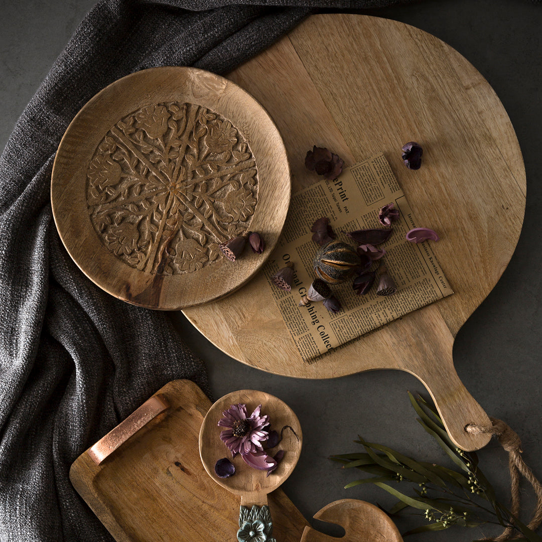 Rustic wooden serving platters and decorative plates with intricate carvings, arranged with dried flowers for a vintage aesthetic.