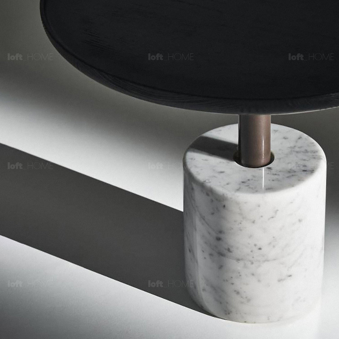 Round black marble table with a white cylindrical marble base, accented by a bronze steel support, ideal for contemporary living spaces.