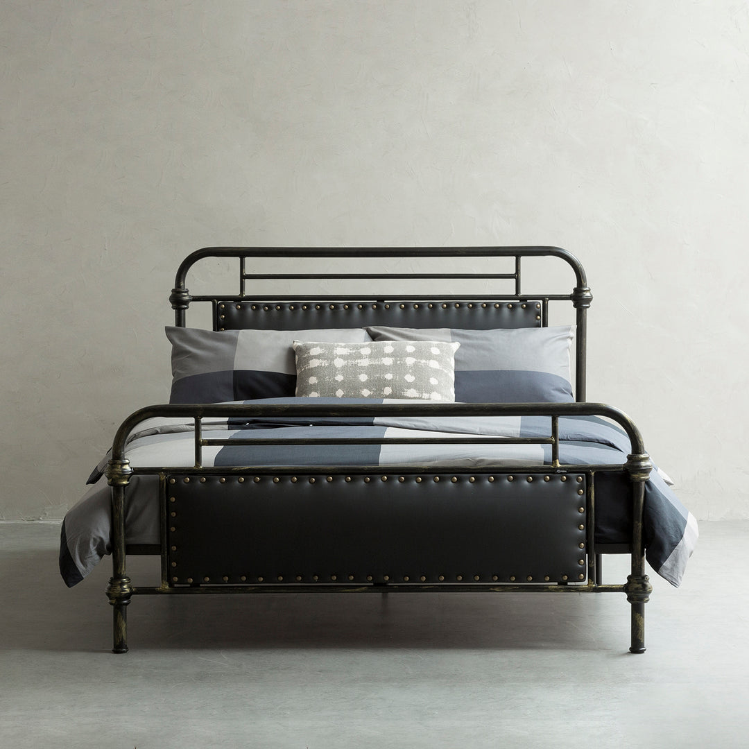 Sturdy metal bed frame with rivet detailing and black leather accents, offering a sleek and industrial style for bedroom decor.