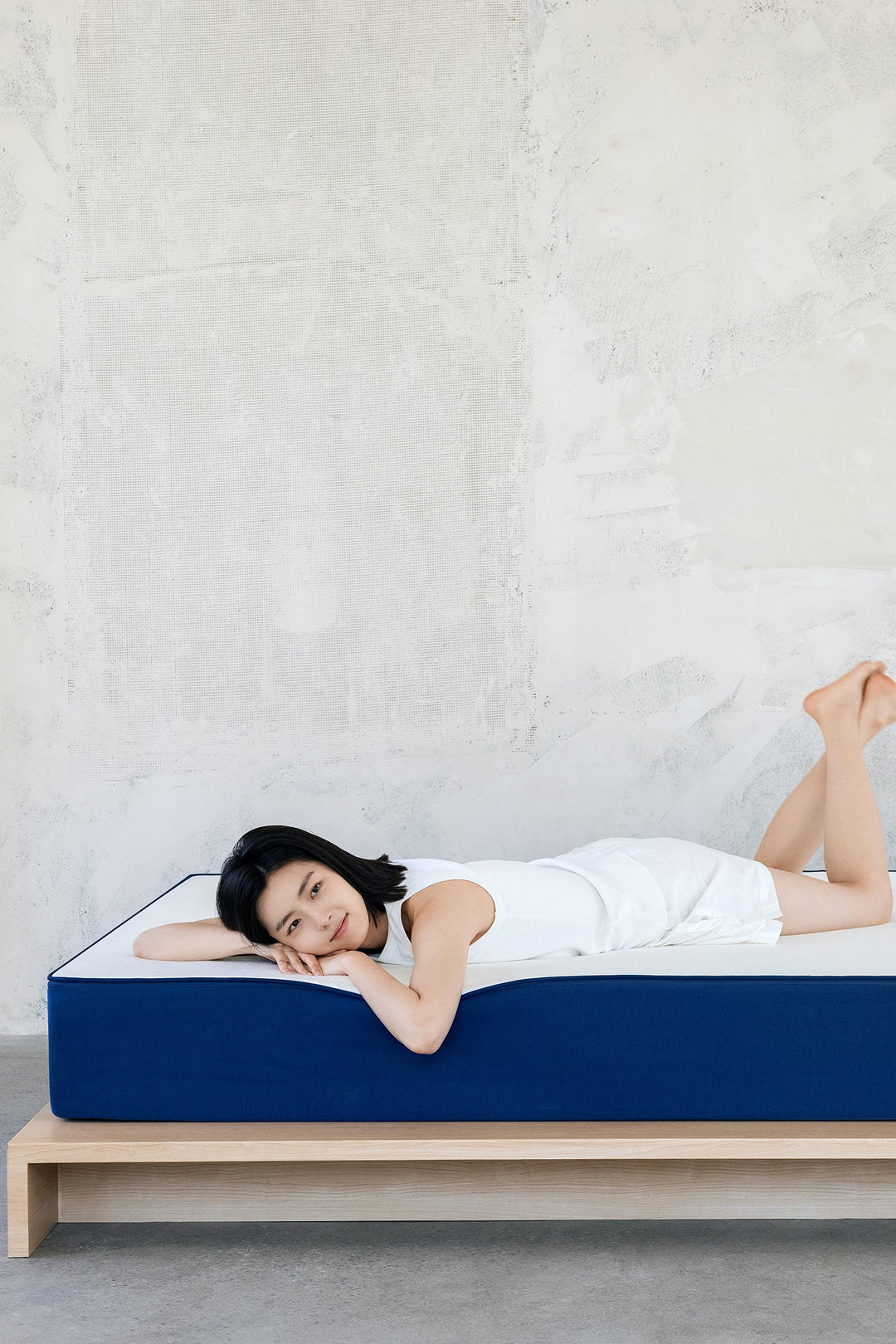 Woman relaxing on minimalist high‑density foam mattress with light wood bed frame, highlighting Loft Home’s premium mattress comfort and clean Scandinavian bedroom style.