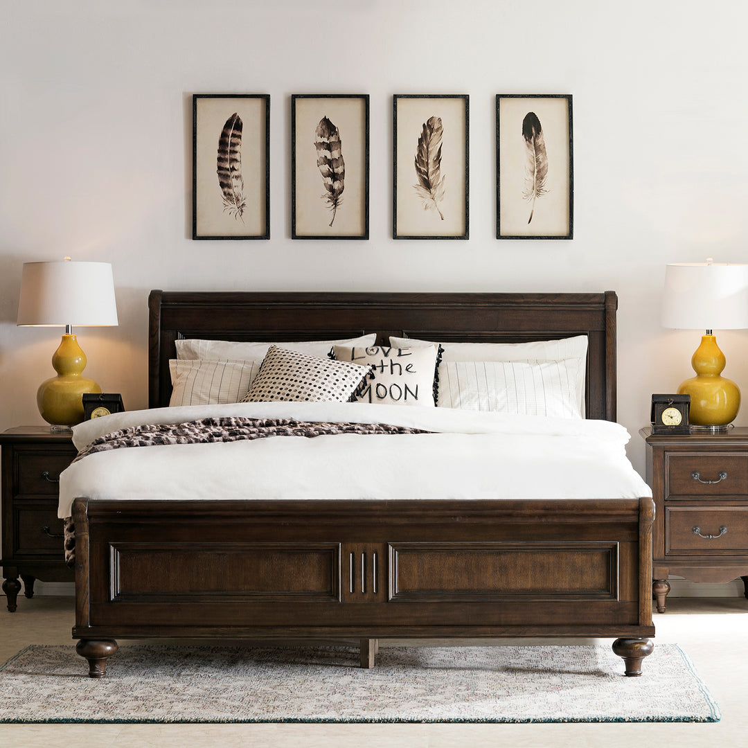 Elegant dark wood bed frame in a cozy bedroom setting, featuring a soft white comforter and decorative pillows. The room is complemented by matching nightstands, yellow table lamps, and framed feather art hanging on the wall above the bed.