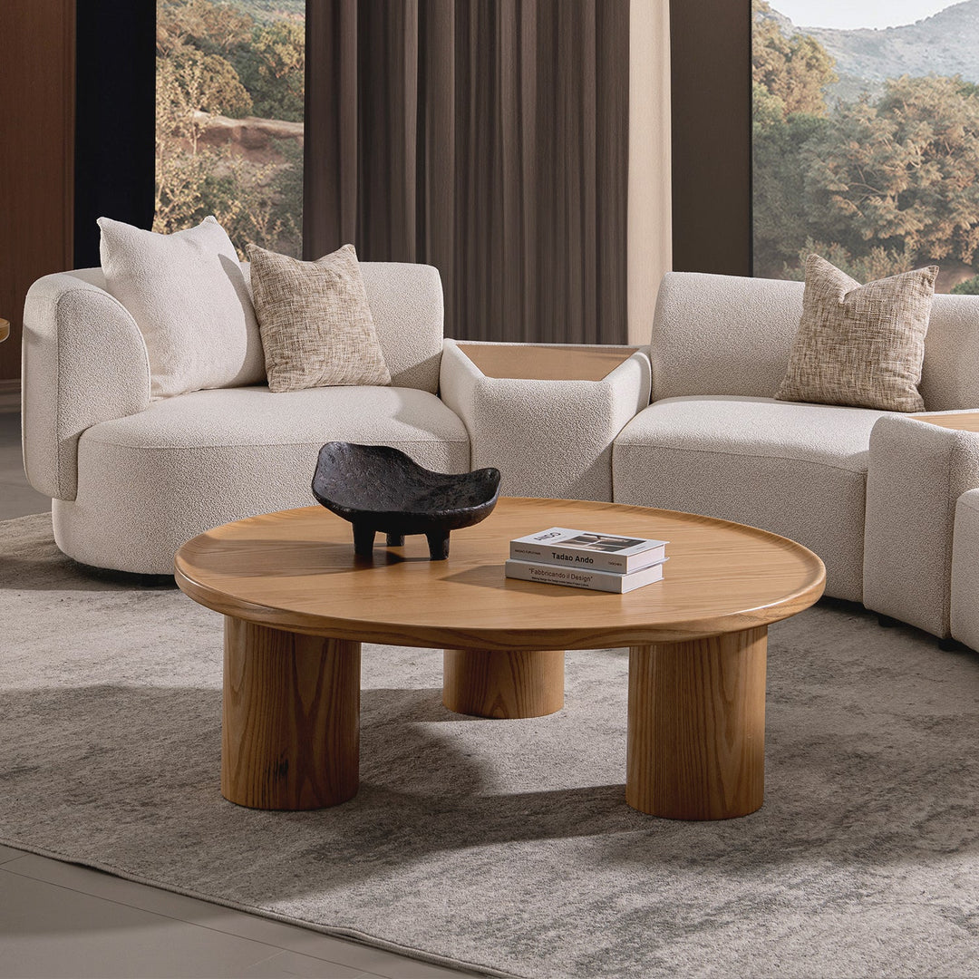 Round wooden coffee table with a natural finish, featuring a minimalist design and sturdy cylindrical legs, complementing cozy living spaces.