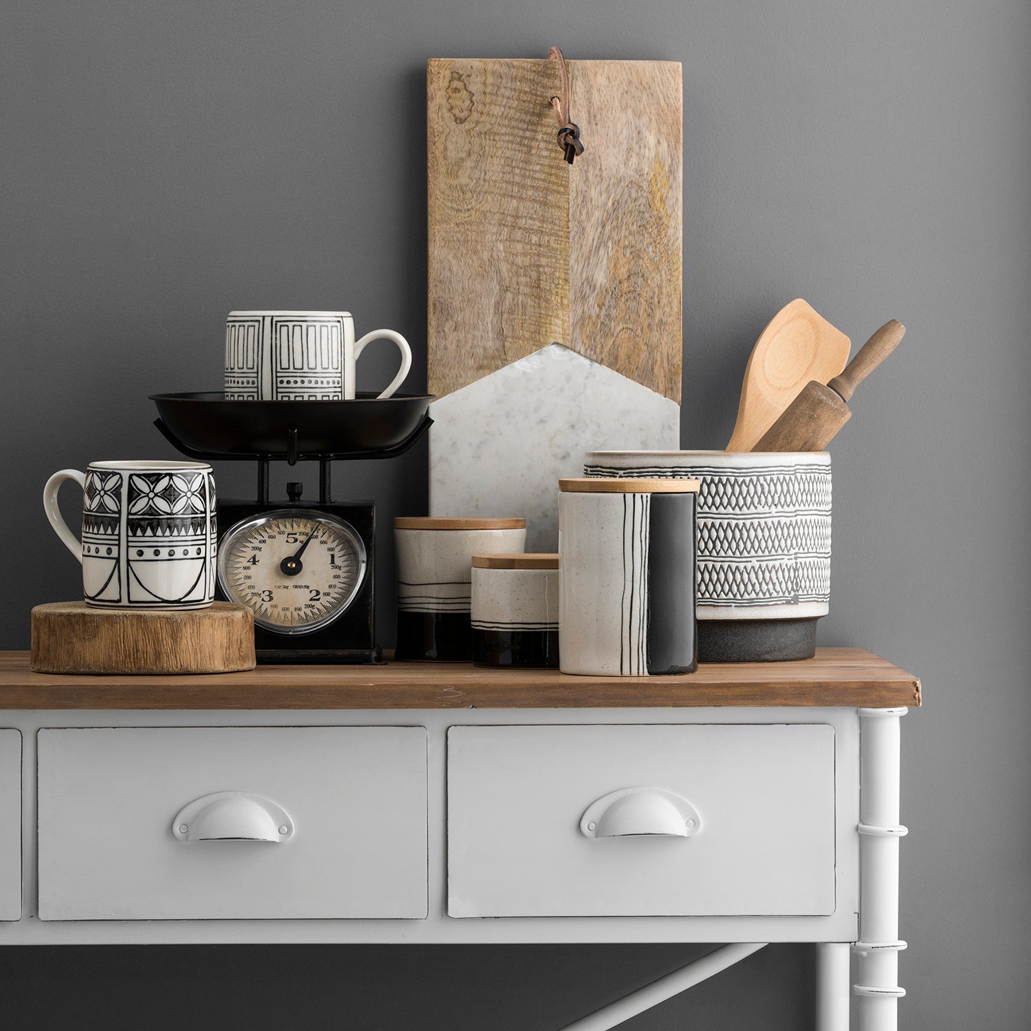 Stylish kitchen decor featuring ceramic jars, patterned mugs, and wooden utensils on a white console table with a rustic wood top. Explore sales by percentage at Loft Home.