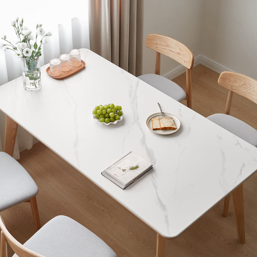 Loft Home sintered stone dining table collection, featuring a marble-patterned table with light wood legs, paired with minimalist chairs, styled with fresh flowers and fruits for a modern and elegant dining setup.