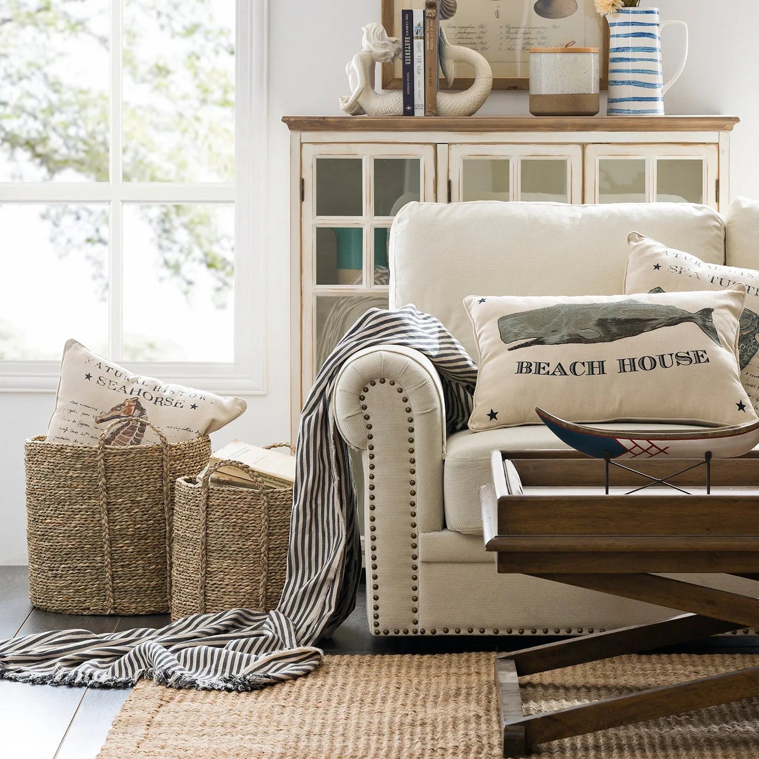 Cozy living room setup featuring a beige sofa with beach-themed pillows, a rustic wooden coffee table, and decorative baskets, linking to Loft Home's sofa by style collection.