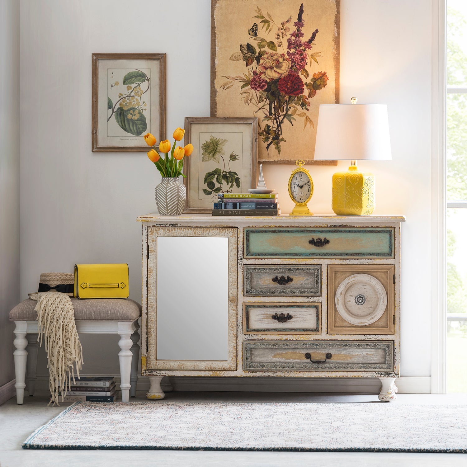 Loft Home vintage-style storage cabinet with distressed finish and colorful drawers, styled with a table lamp, framed artwork, and floral accents, enhancing eclectic home decor.