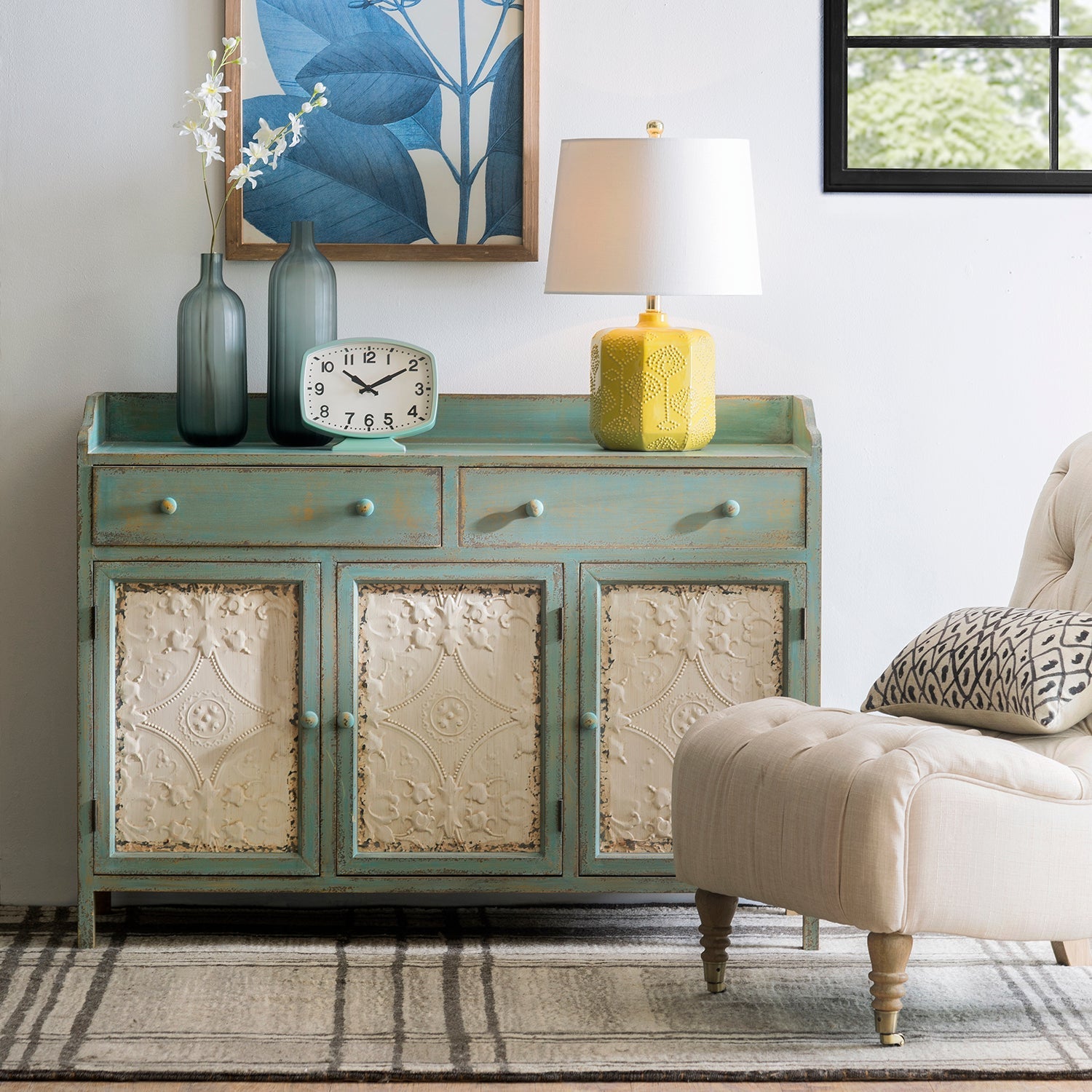 Loft Home vintage-style storage cabinet with distressed teal finish and ornate white paneling, styled with a yellow lamp and decorative vases, perfect for adding charm to classic interiors.