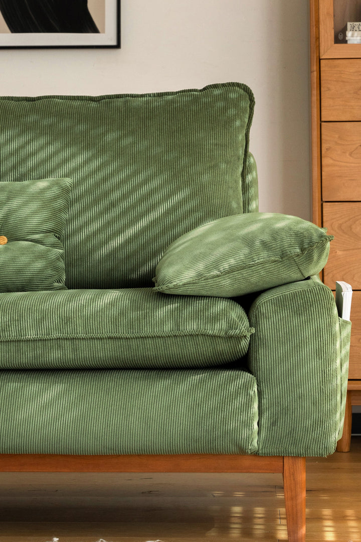 Green corduroy fabric sofa with wooden legs in a living room. Loft Home fabric sofa featured product.