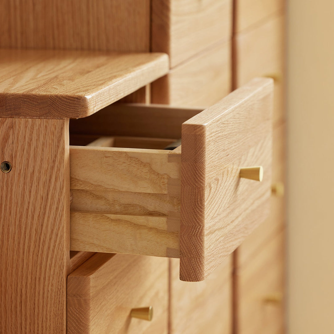 Close-up of a wooden chest of drawers, showcasing smooth craftsmanship and a partially open drawer with sleek gold handles, blending elegance and functionality for home storage.