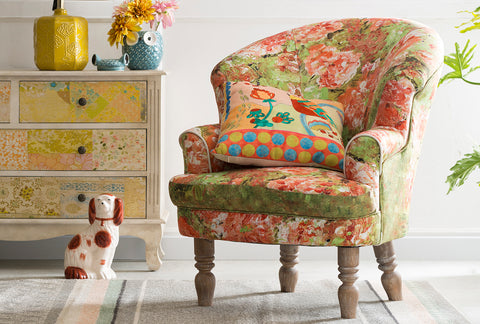 Vibrant floral-patterned 1-seater sofa with colorful cushion, placed in a charming living room with an eclectic dresser and decorative accents, linking to Loft Home's 1-seater sofa collection.