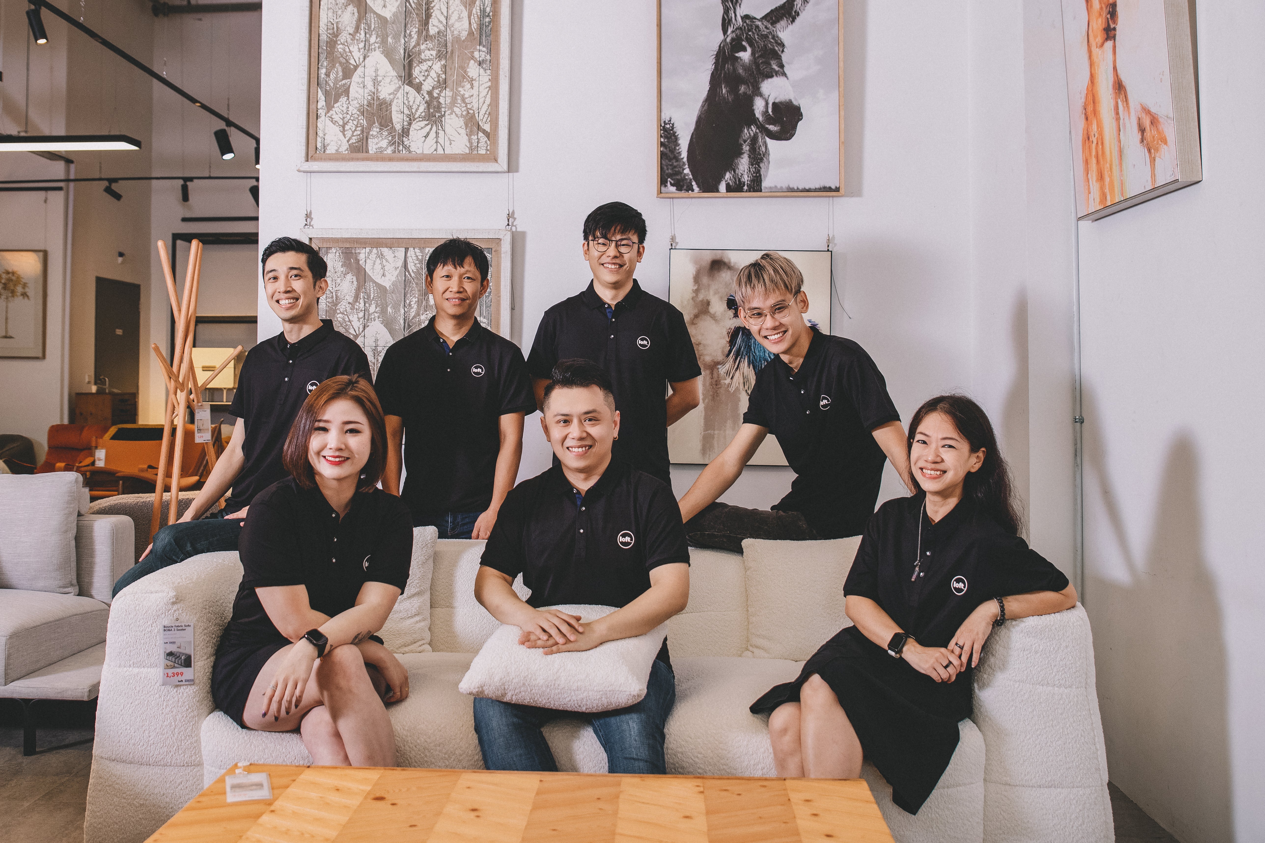 The Loft Home team proudly sitting in a modern furniture showroom, showcasing their dedication to quality and service. Meet our team at Loft Home.