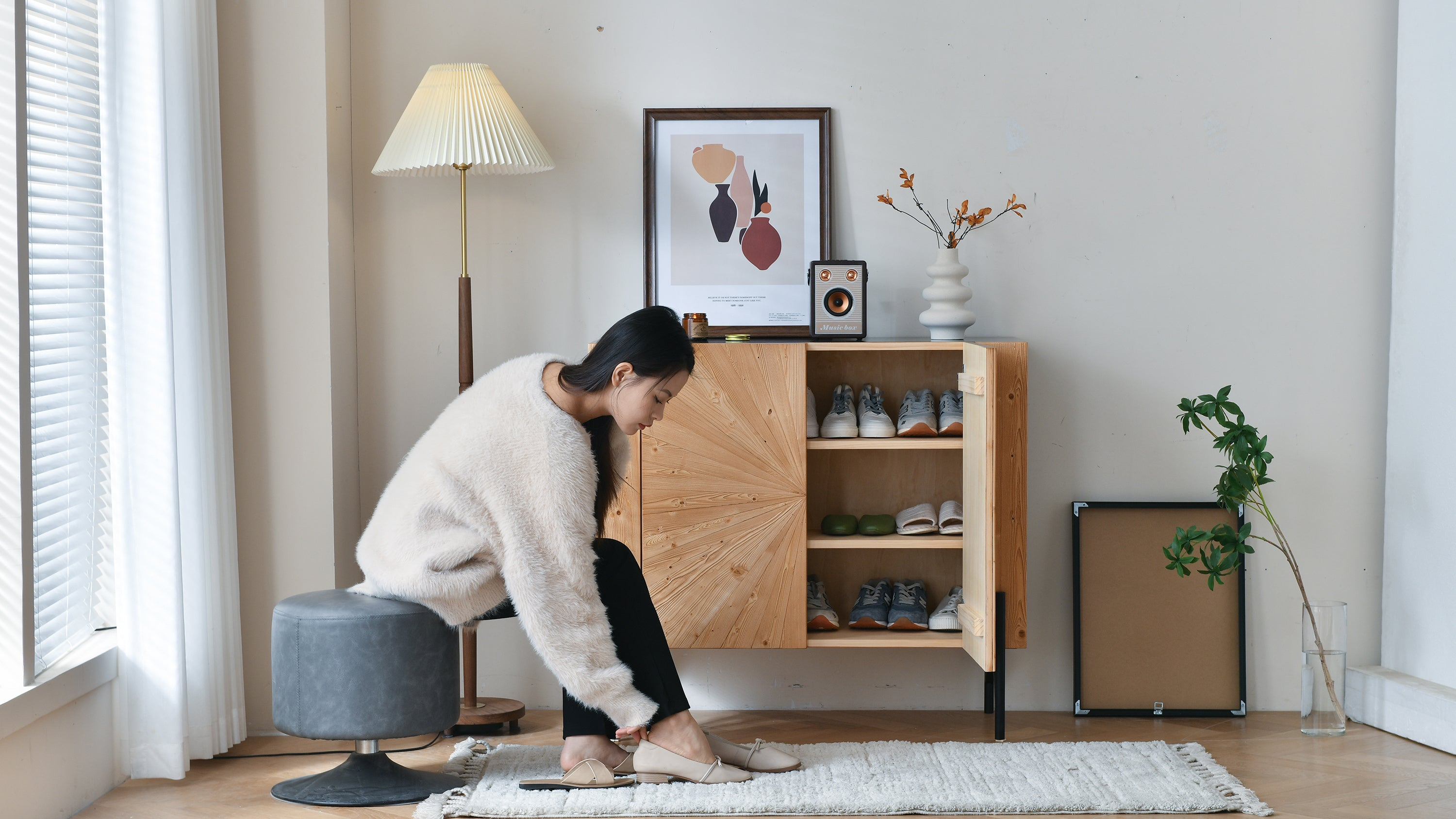 Loft Home entrance area featuring a woman putting on shoes by a wooden shoe cabinet, with stylish decor and natural light.