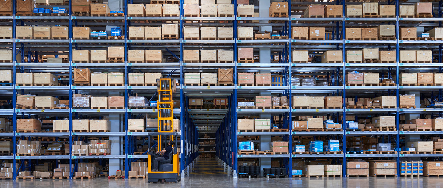 Large warehouse with multiple shelves filled with boxes and a forklift in the center.