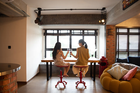 Two people enjoying drinks at a modern wooden table, creating cozy vibes in a stylish loft interior for Loft Home's New Homeowners Promo.