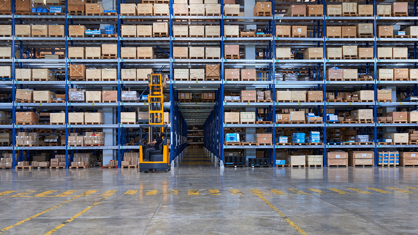 Large warehouse with high shelves filled with boxes and a forklift in the center.