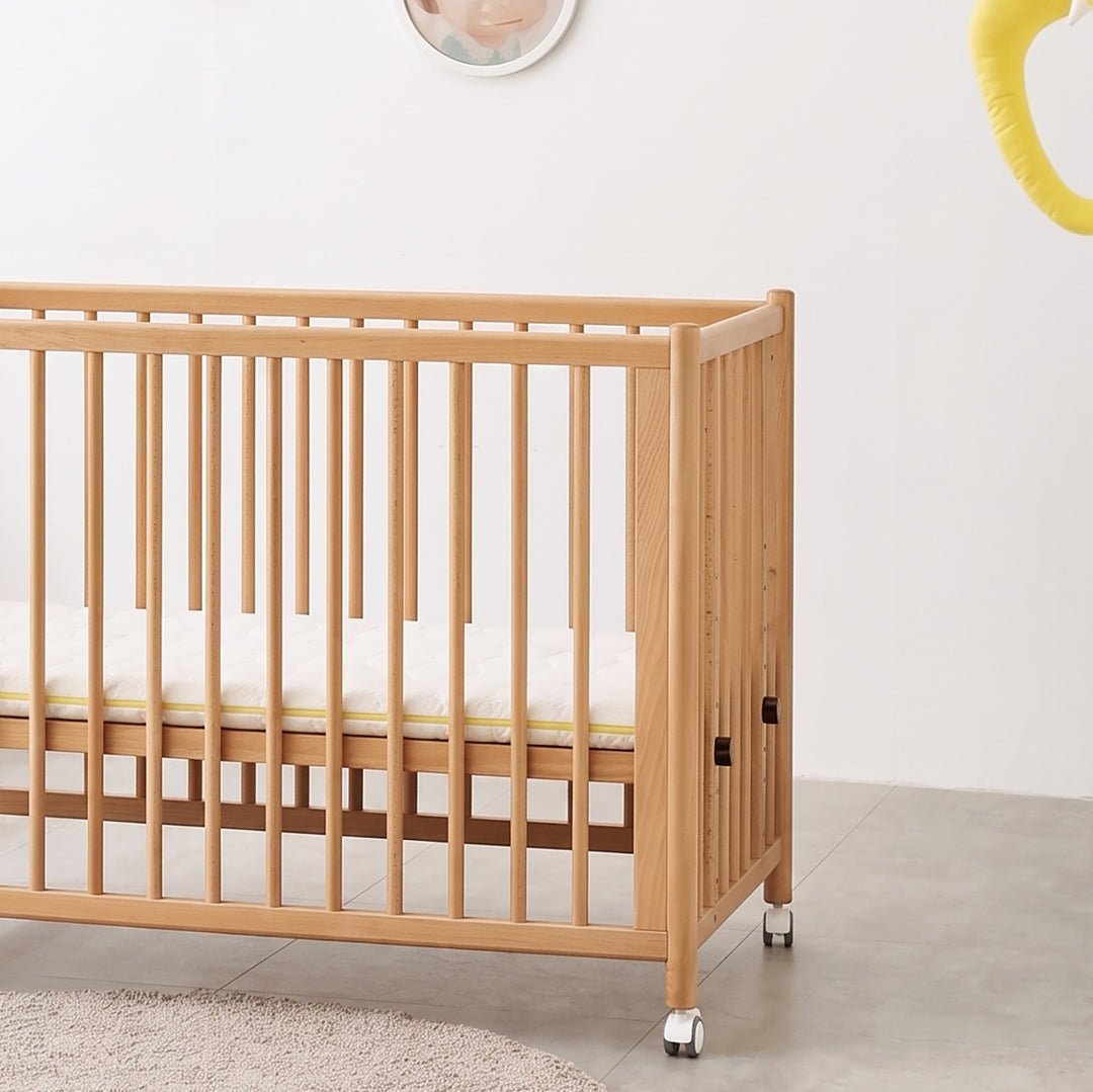 Scandinavian beech wood bed side baby crib with wheels ember in panoramic view.