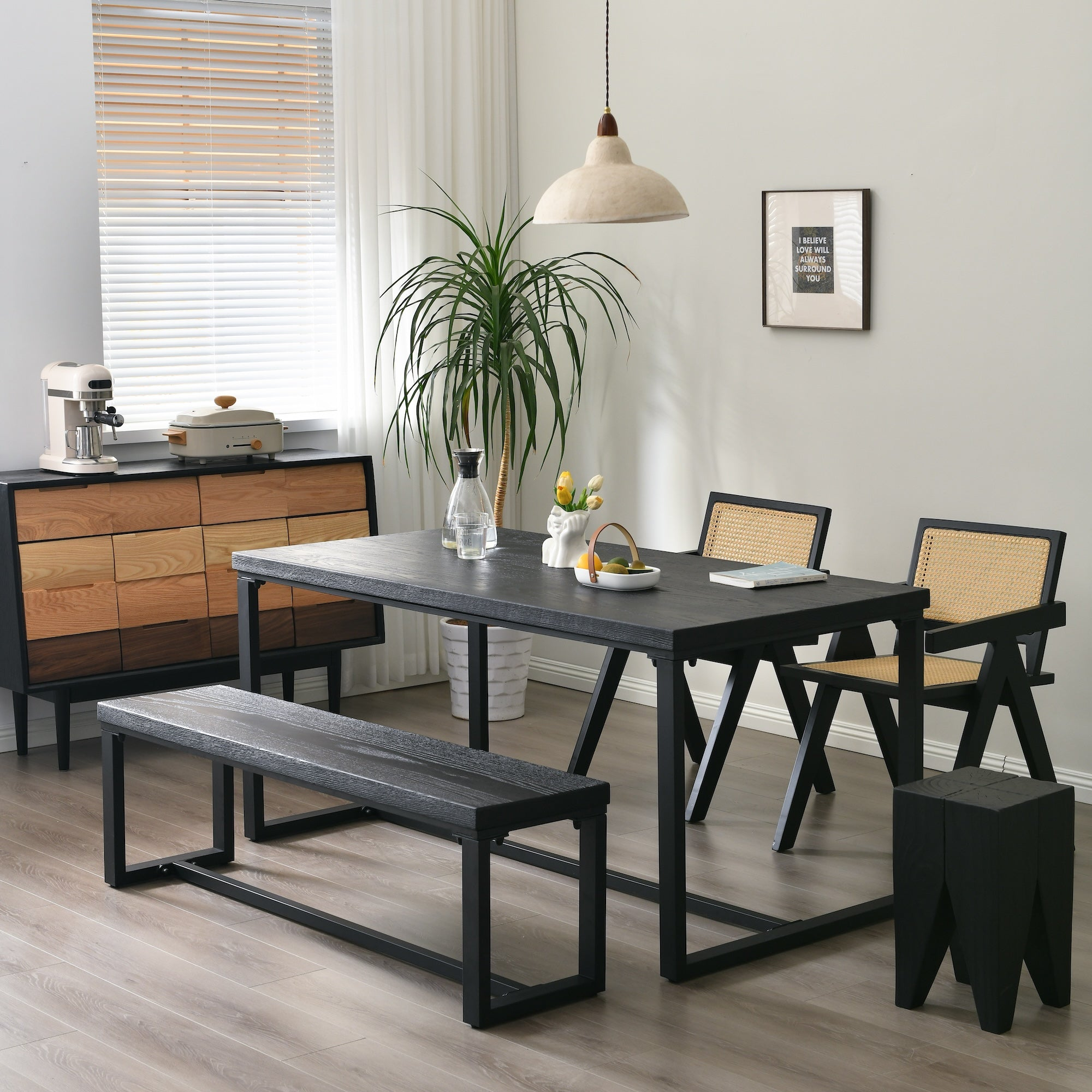 Modern dining area with a black wooden table, matching bench, rattan chairs, sideboard, potted plant, and pendant light, creating a contemporary and inviting space.