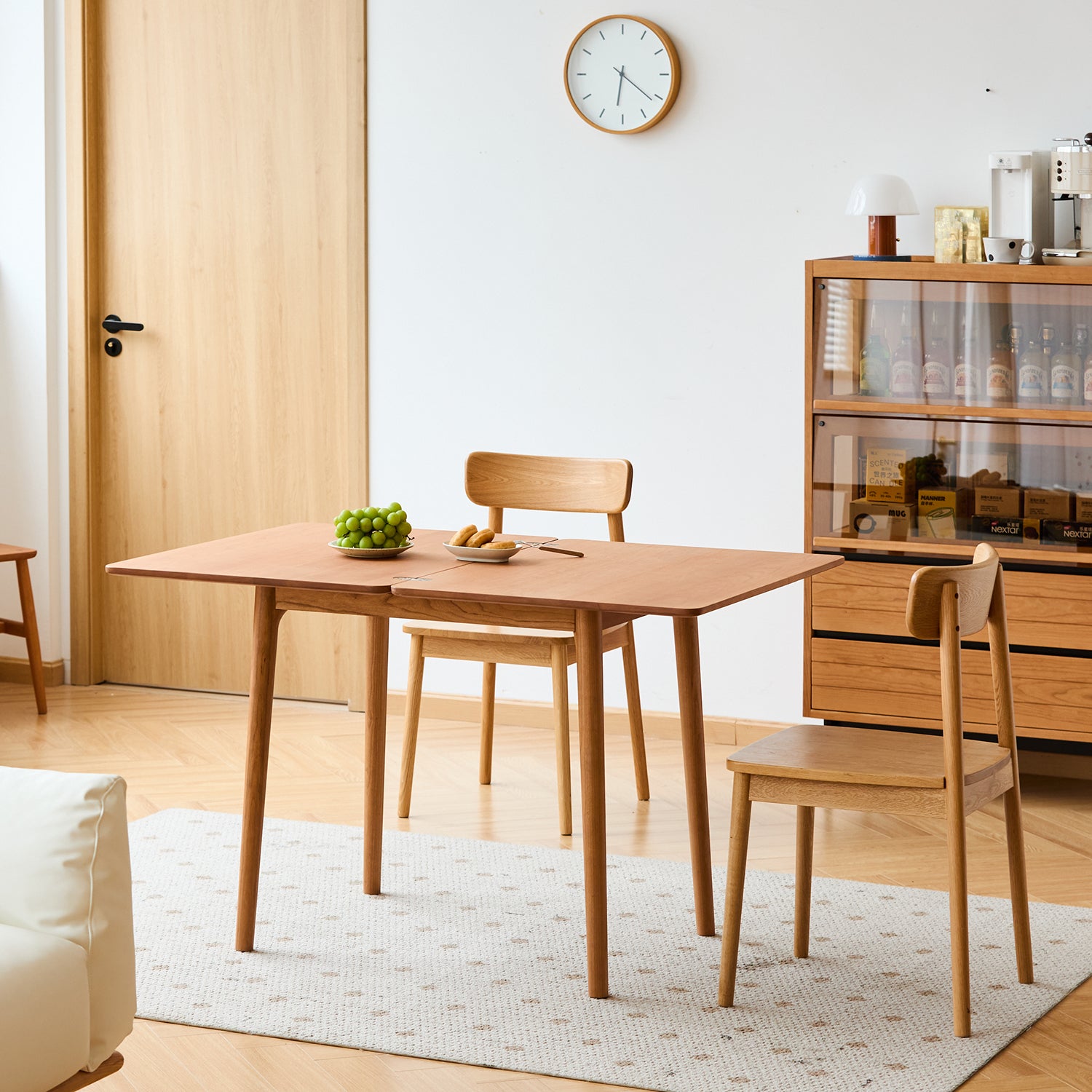 Wooden dining table with chairs in a room with a clock on the wall and a cabinet.