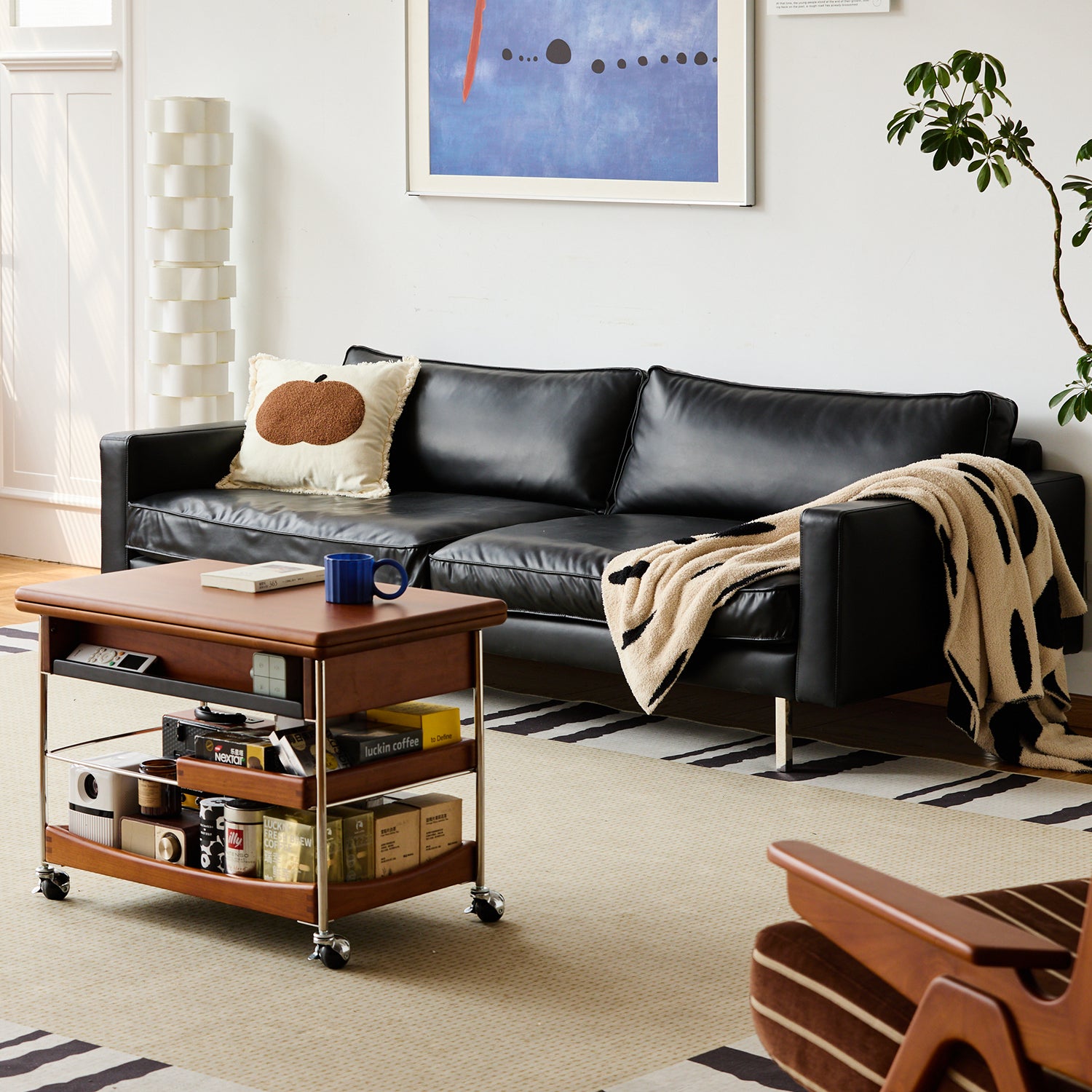 Black leather sofa styled with a cozy throw and cushion, paired with a wooden coffee trolley, creating a warm modern Loft Home living room setup.