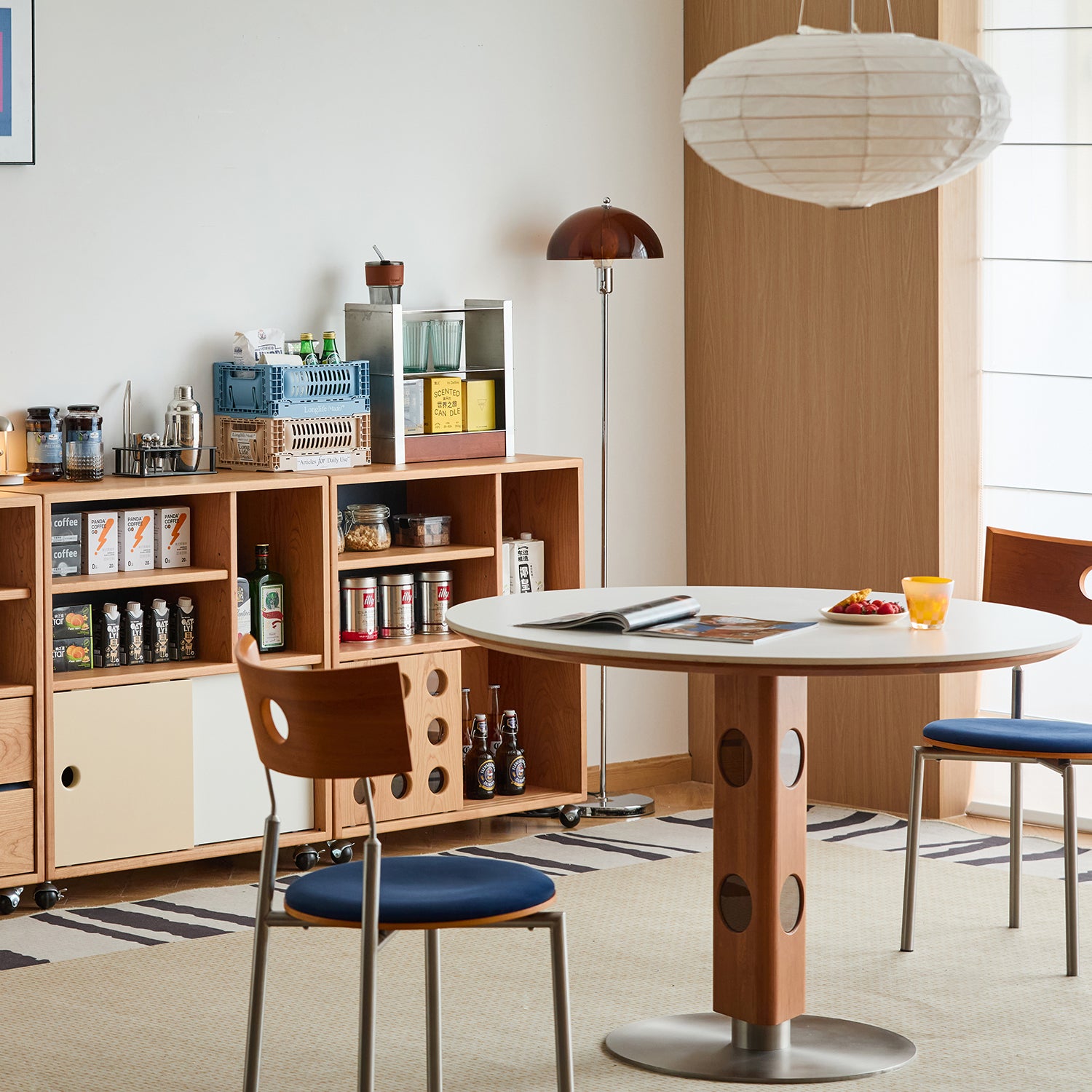Modern round dining table with wooden pedestal and matching chairs in a cozy Scandinavian-style home setting, styled with open storage shelves and warm natural tones enhancing Loft Home interior charm.