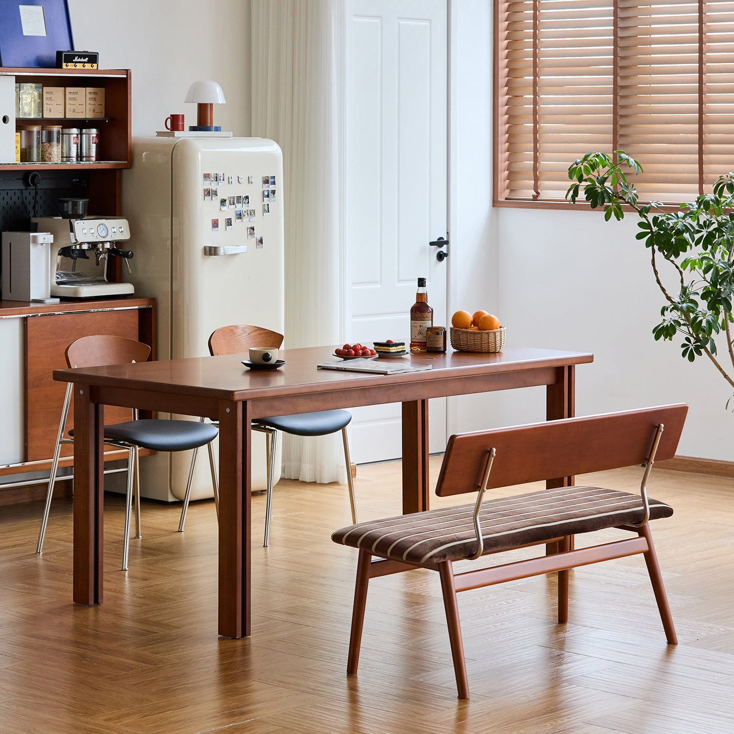 Vintage boxwood dining table paired with curved chairs and a cushioned bench, styled with a retro fridge and wood-accented pantry, enhancing a nostalgic yet refined kitchen space.